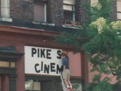 A fitter on a ladder fixes letters across a cinema fascia.