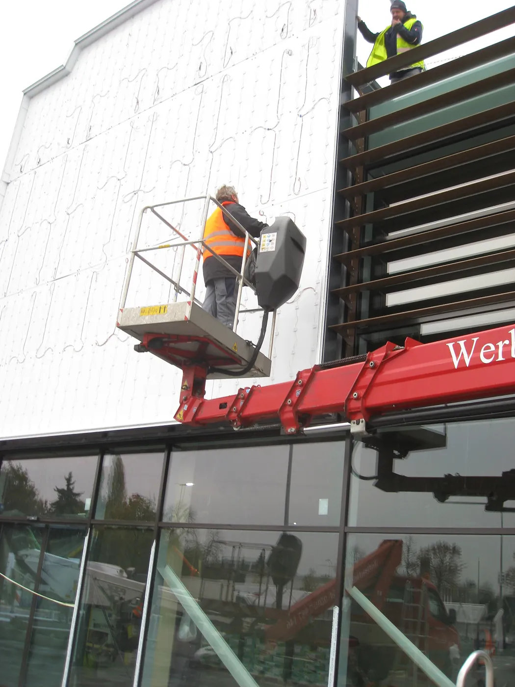 Installers on a lift fixing a large sign to a building.
